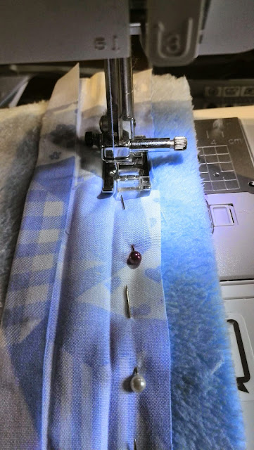 Naaimachine stikt biaislint op blauwe fleece met spelden vastgezet