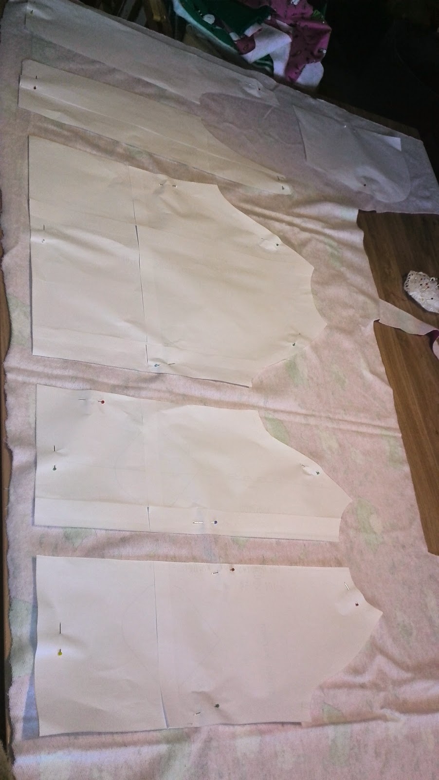 Patroononderdelen van de hoodie opgespeld op de roze stof, klaar om te knippen