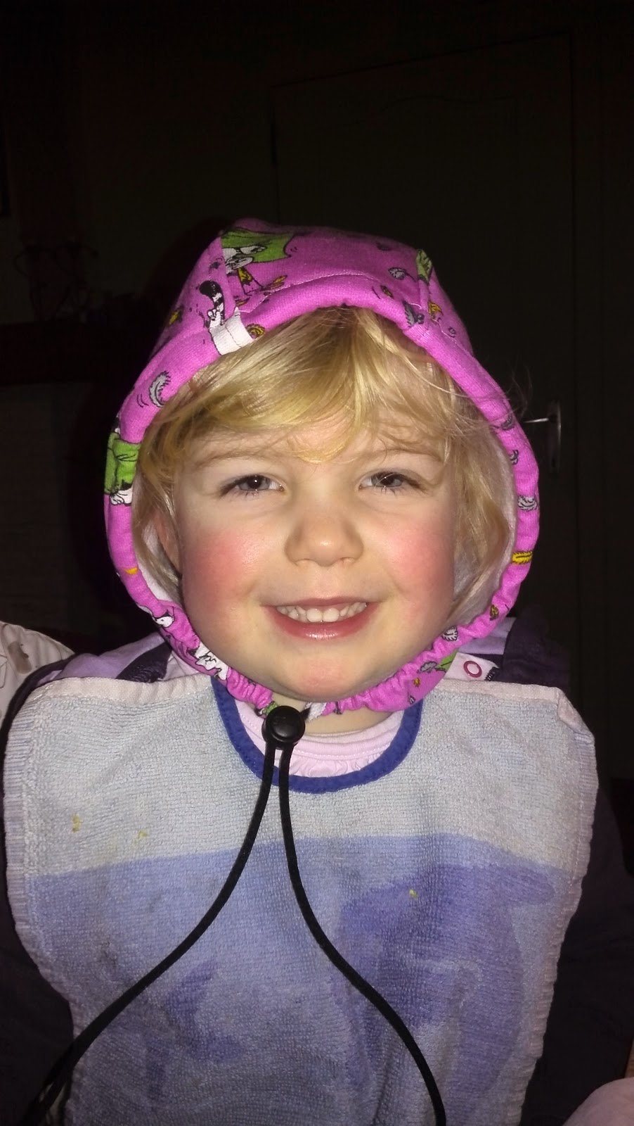 Blond meisje lacht breed met het roze kapje van de hoodie al op haar hoofd