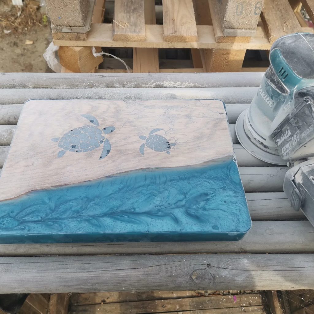 Tapasplank met epoxy oceaanmotief en schildpadden tijdens tussenschuren met excenterschuurmachine.