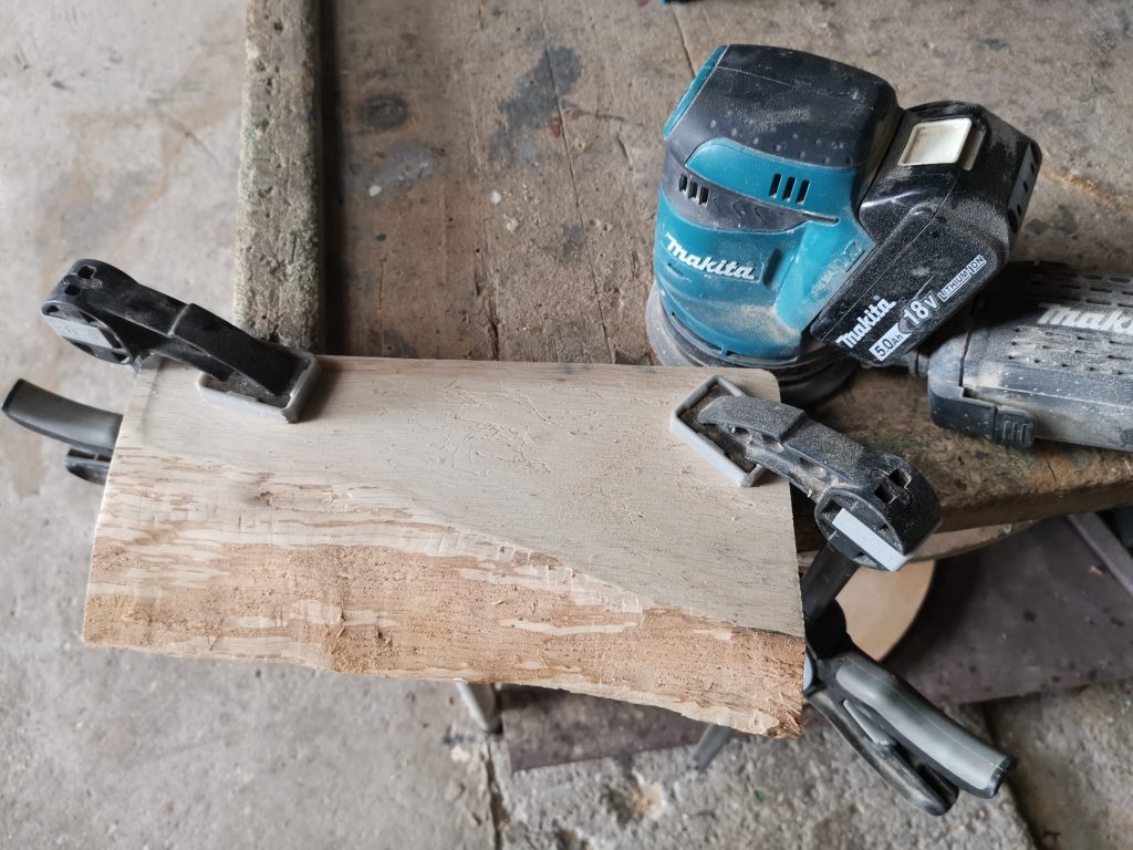 Ruwe houten tapasplank vastgeklemd tijdens het schuren met excenterschuurmachine.