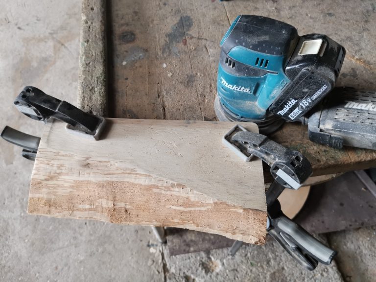 Ruwe houten tapasplank vastgeklemd tijdens het schuren met excenterschuurmachine.