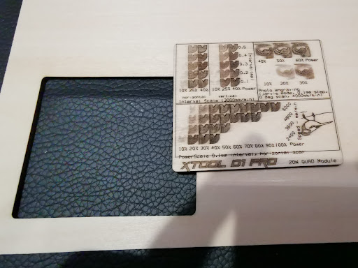 Testkaart met laserinstellingen gegraveerd op hout, geplaatst op een leerstructuur achtergrond.