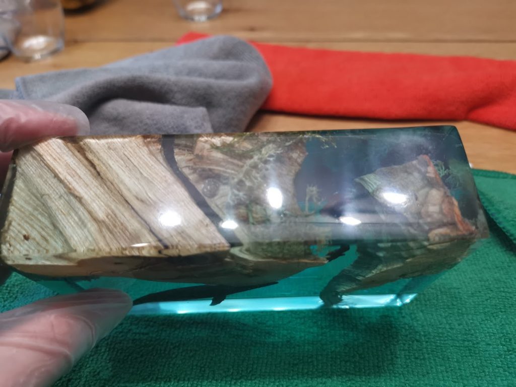 Klein drijfhout blokje ingegoten in turquoise transparante epoxy, hand houdt het vast