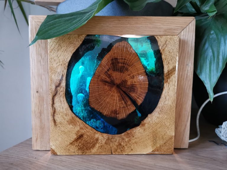 Eiken lamp met ingezette boomschijf omgeven door turquoise donkerblauw epoxy met kwallenpatroon, van achteren verlicht