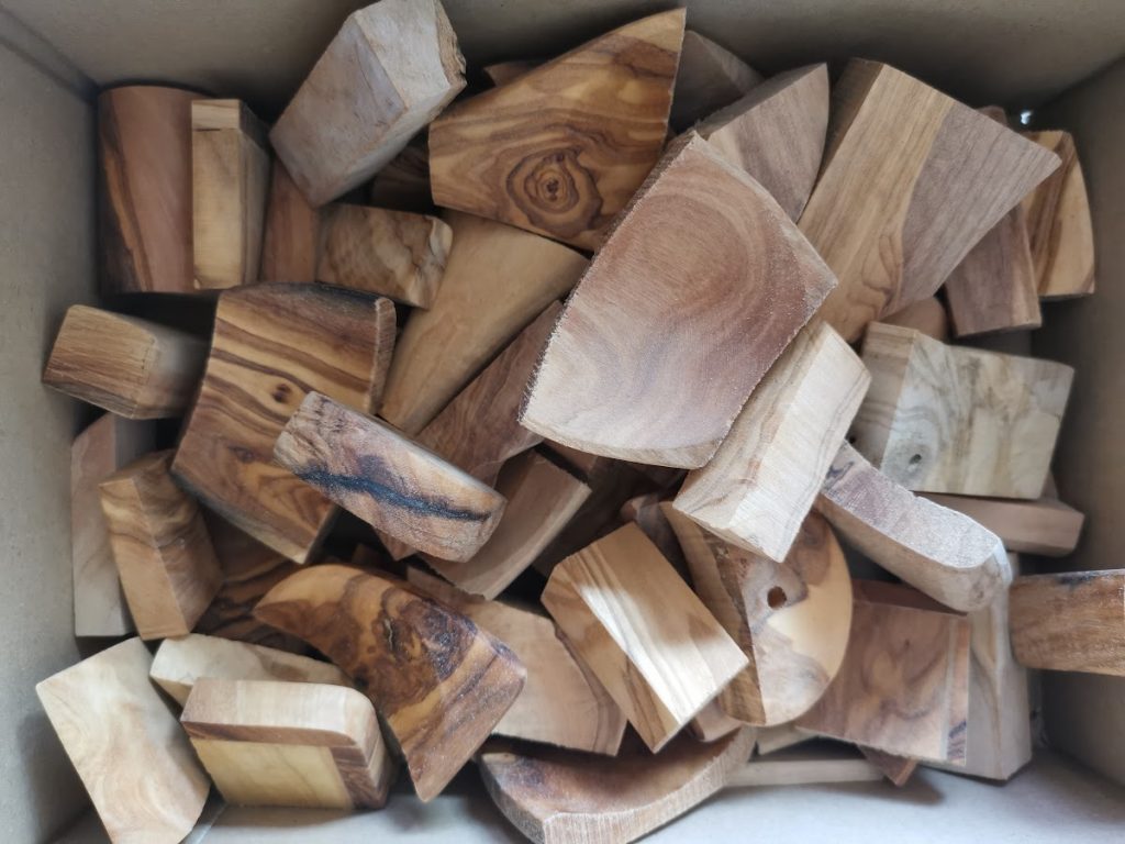 Doos vol olijfhout restjes in verschillende grillige vormen met warme bruingouden tekening