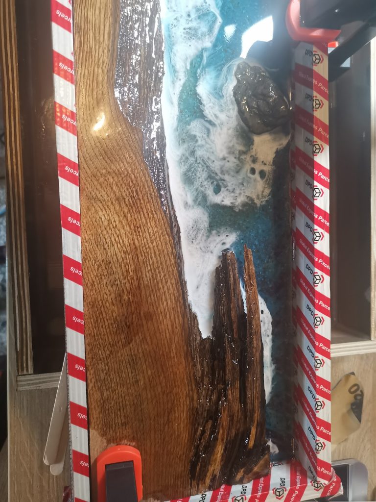 Eiken plank met drijfhout en blauw oceaan epoxy in een mal tijdens het gieten