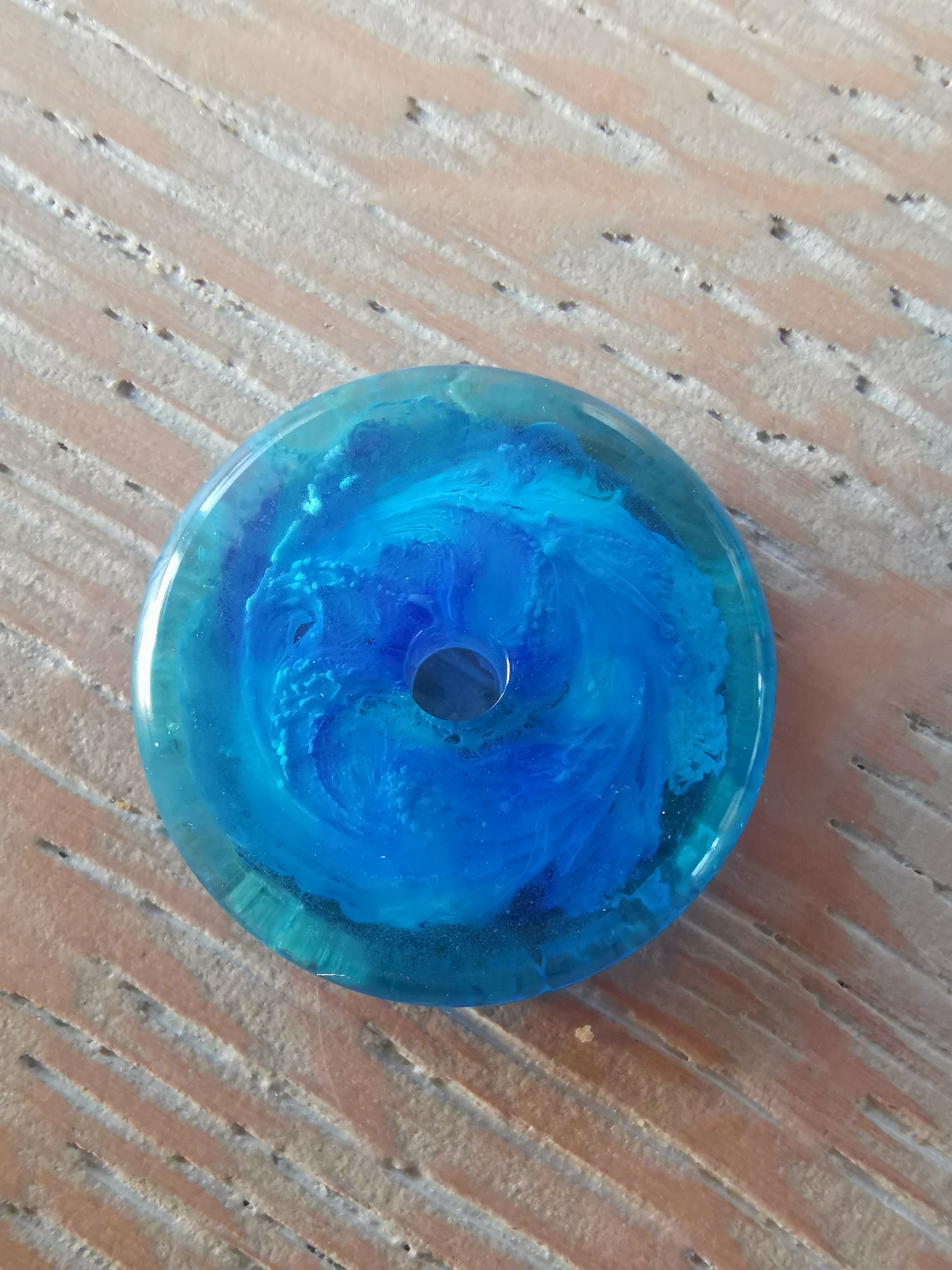 Close-up van een blauwe resin donut met een swirl van teal en diepblauw, gemaakt van harsresten