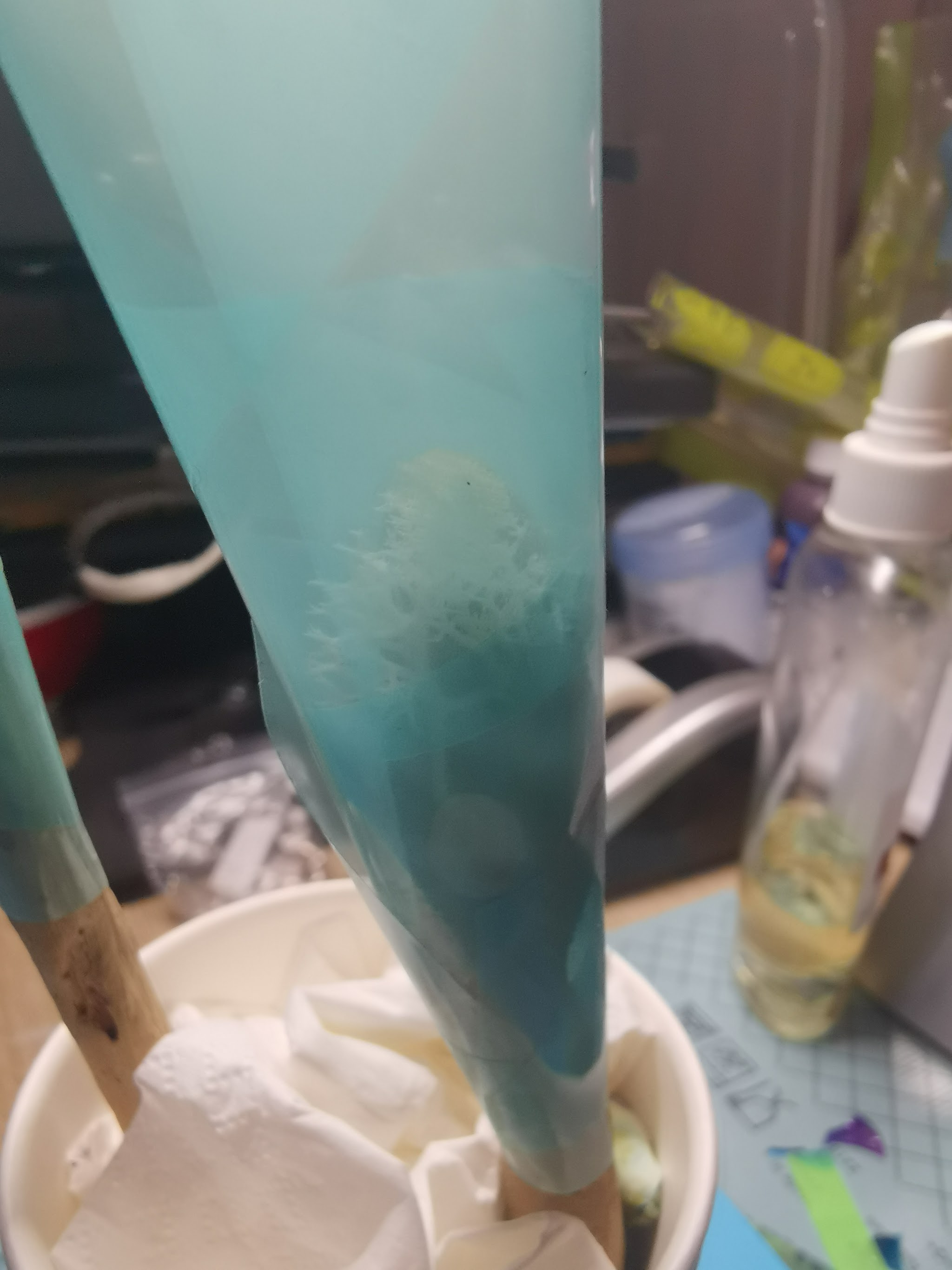 Drijfhout hairpins rechtop gezet in piepschuim terwijl de bovenkant uithardt — mengbekers met resin op de achtergrond zichtbaar