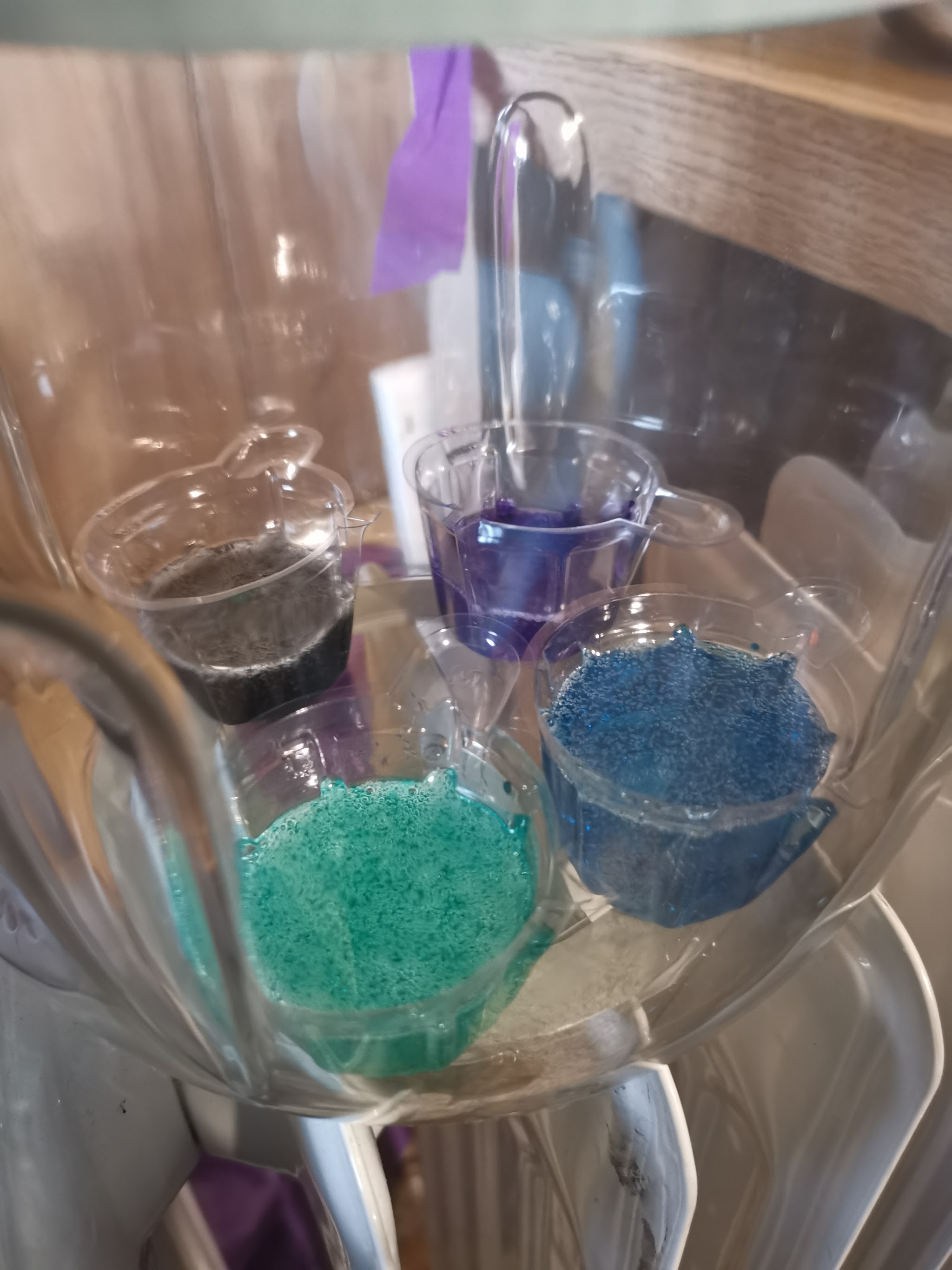Mengbekers met gekleurde epoxyhars (teal, blauw, paars en zwart) in de Resiners debubbler — bellen komen naar de oppervlakte terwijl de vacuüm ze eruit trekt
