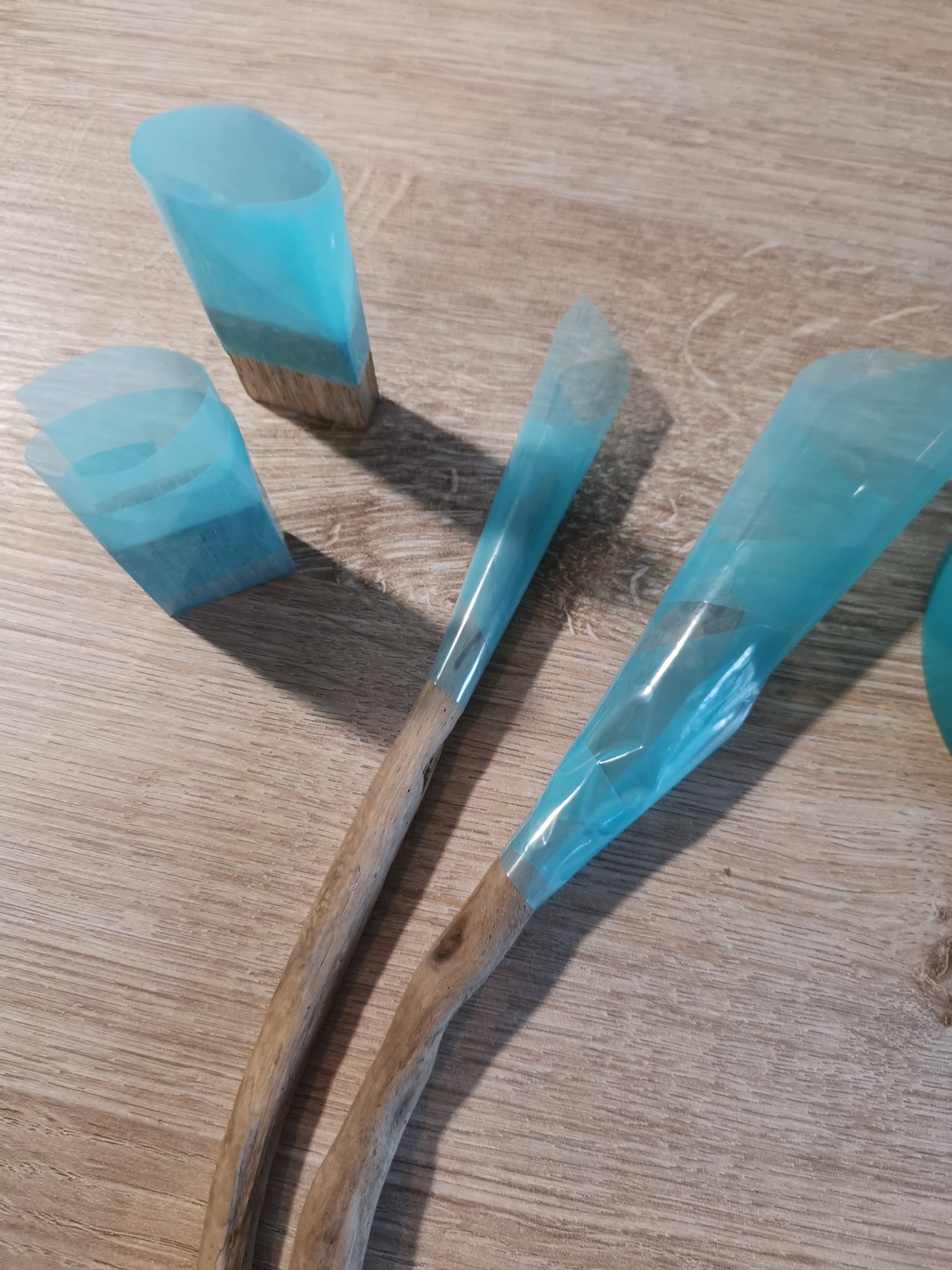 Drijfhout hairpins en eikblokjes liggend op houten tafel: de bovenkant-uiteinden zijn gewikkeld in resintape mallen en gevuld met teal resin — de punten zijn nog kaal hout