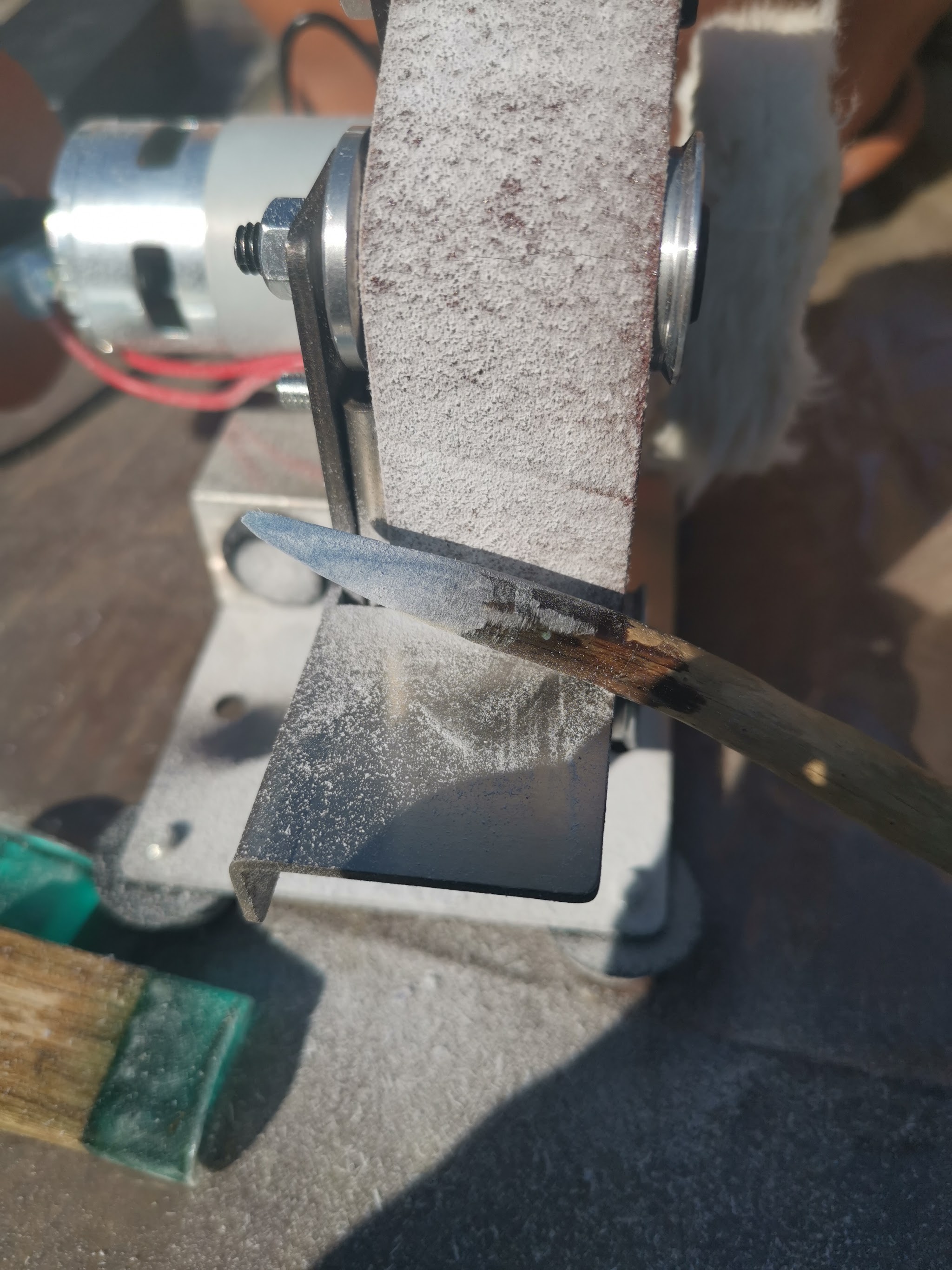 Close-up van een hairpin punt op de schuurband van de mini bandschuurmachine — de resin punt wordt gevormd en overtollig hars bijgeschuurd