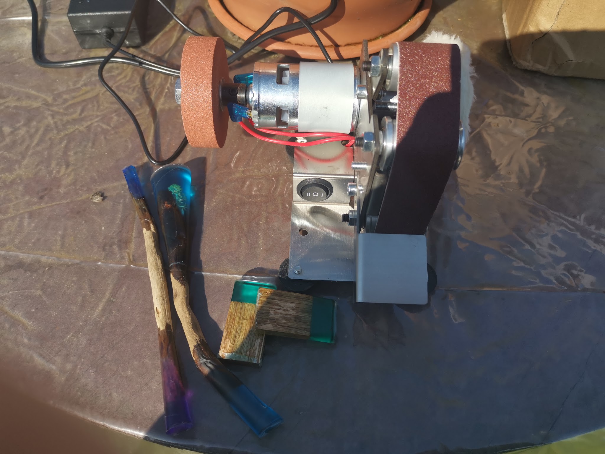 Mini bandschuurmachine met schuurband en slijpschijf, drijfhout hairpins en eikblokjes liggen klaar voor bewerking