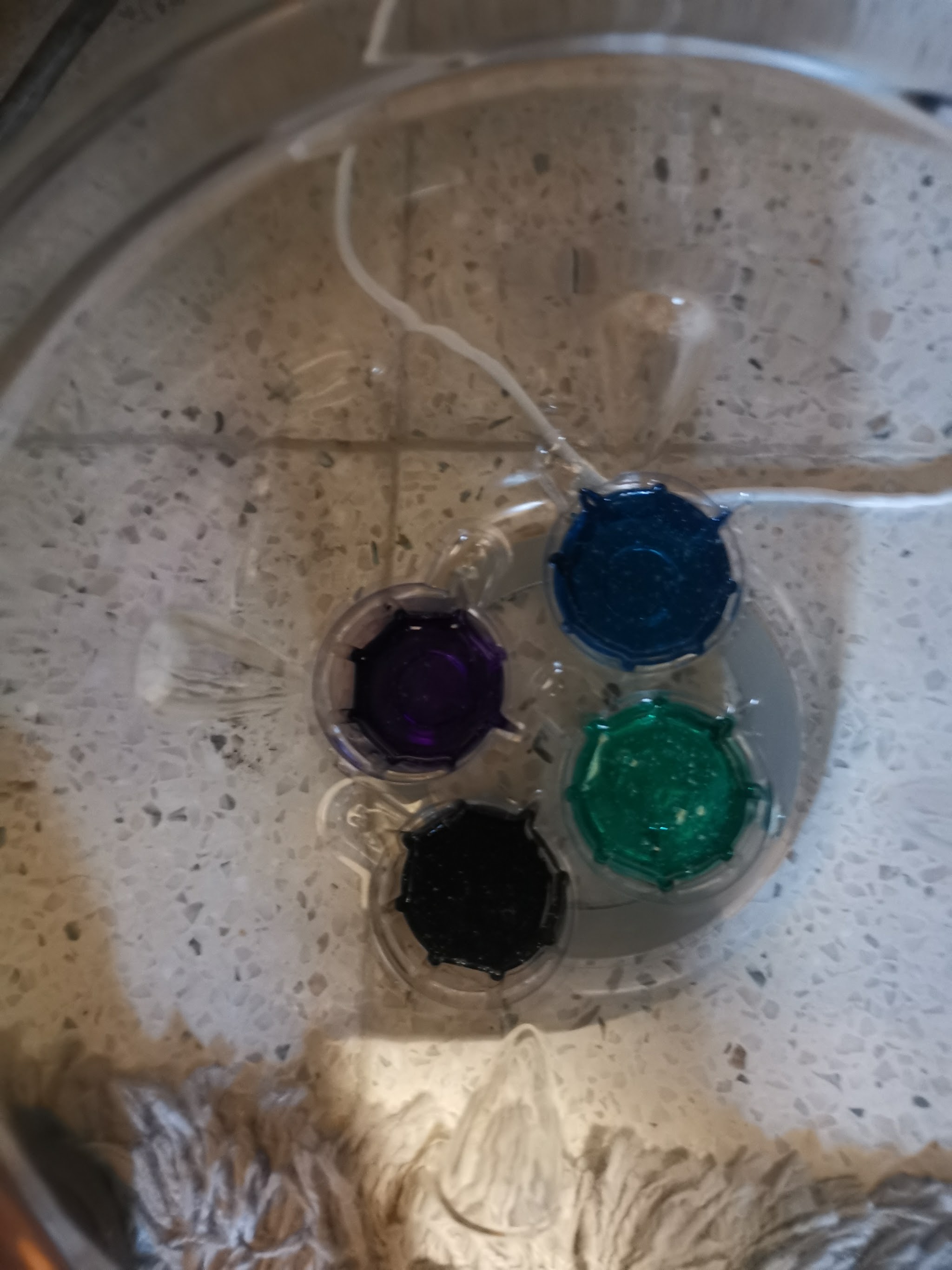 Vier potjes gekleurde resin dye (paars, blauw, groen en zwart) van bovenaf gezien in de vacuümkamer van de Resiners debubbler