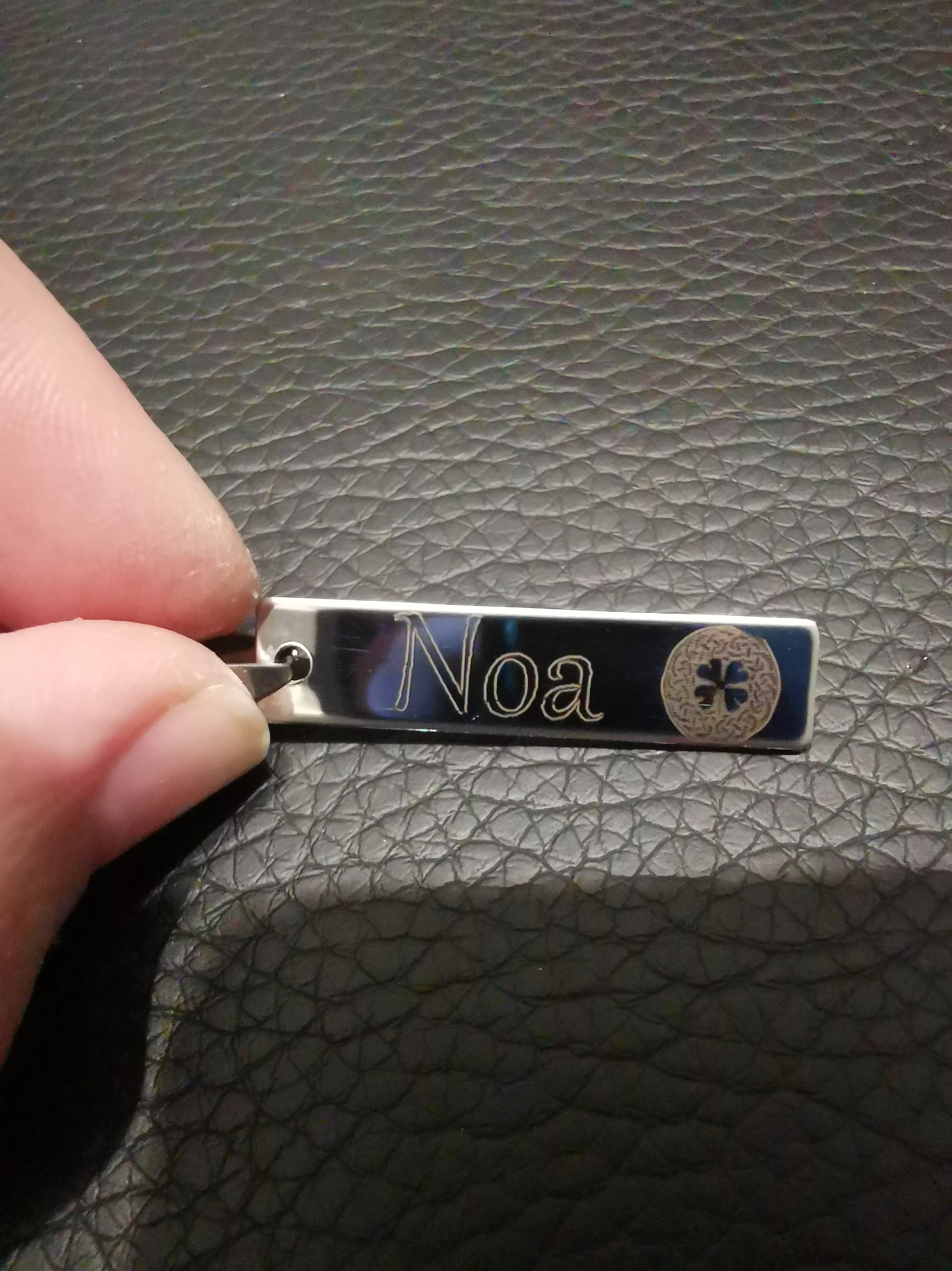 Rechthoekige metalen hanger gehouden in hand, gegraveerd met naam Noa en klein decoratief symbool