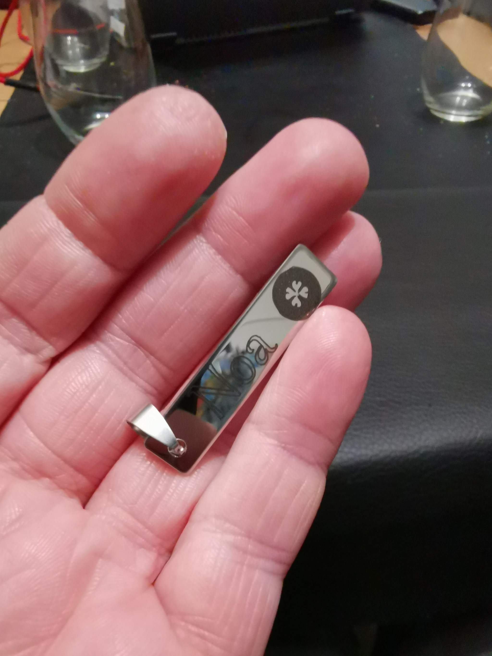 Donkere metalen hanger aan koord, met licht gegraveerde tekst op geanodiseerd aluminium oppervlak