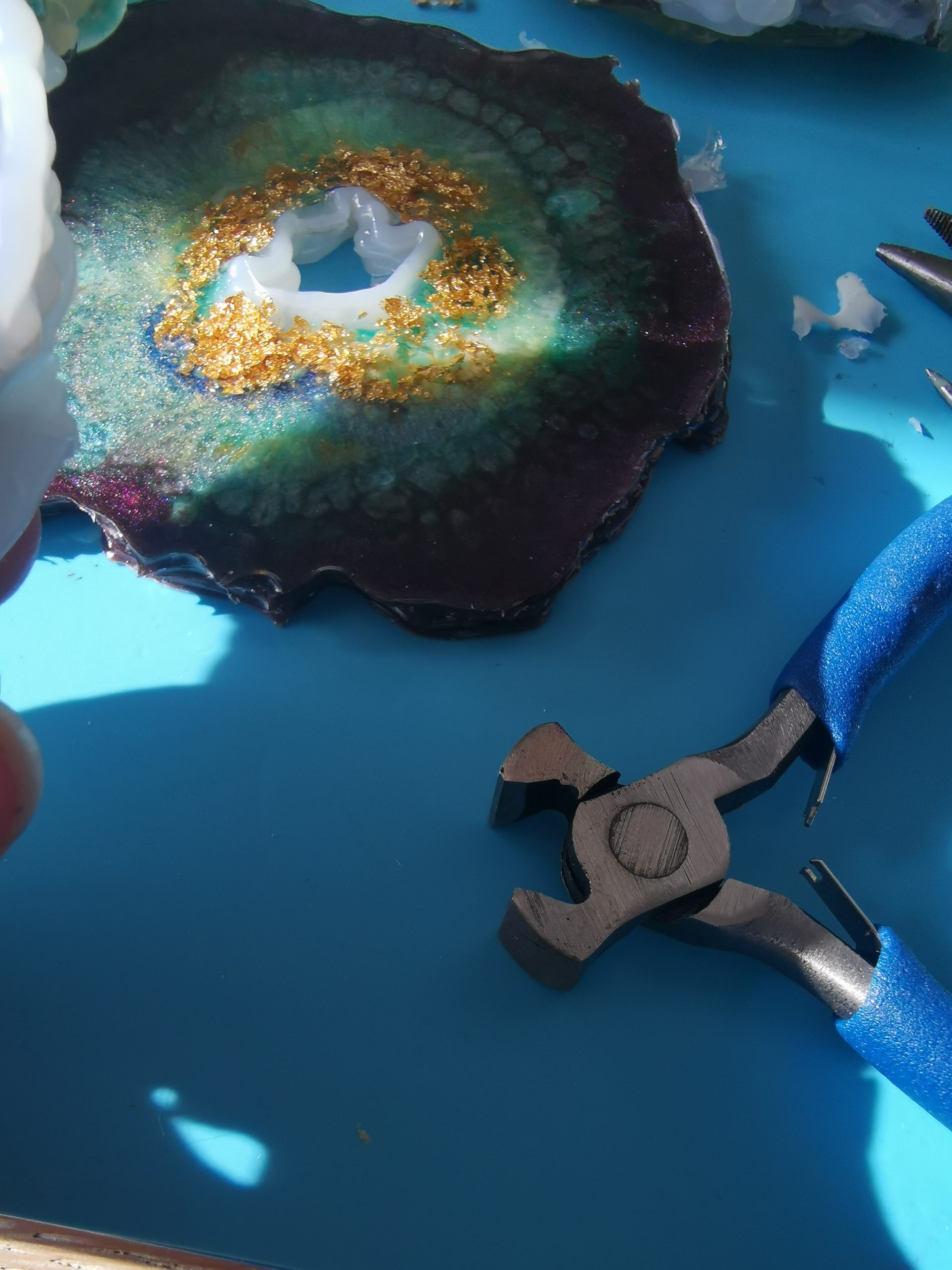 Tang naast de coaster en losse hotlijmstukjes op de mat — bewijs van de mislukte verwijderpoging