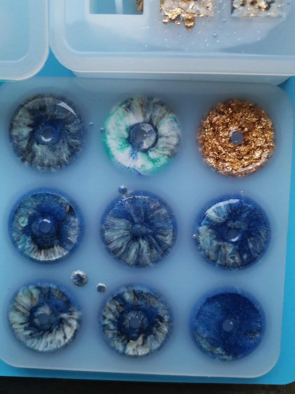 Close-up of the silicone mold with nine round donut-shaped resin beads in blue petri dish style
