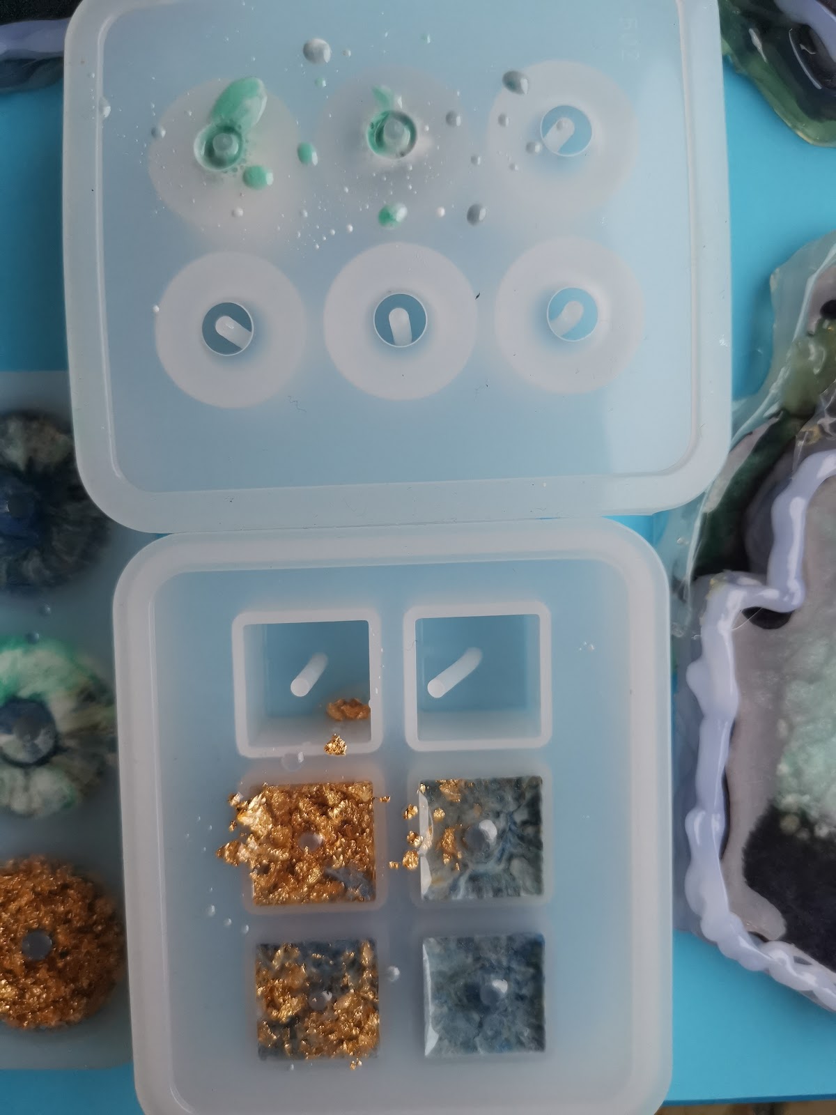 Two silicone molds: round donut mold with freshly poured resin and square mold with gold and blue pieces