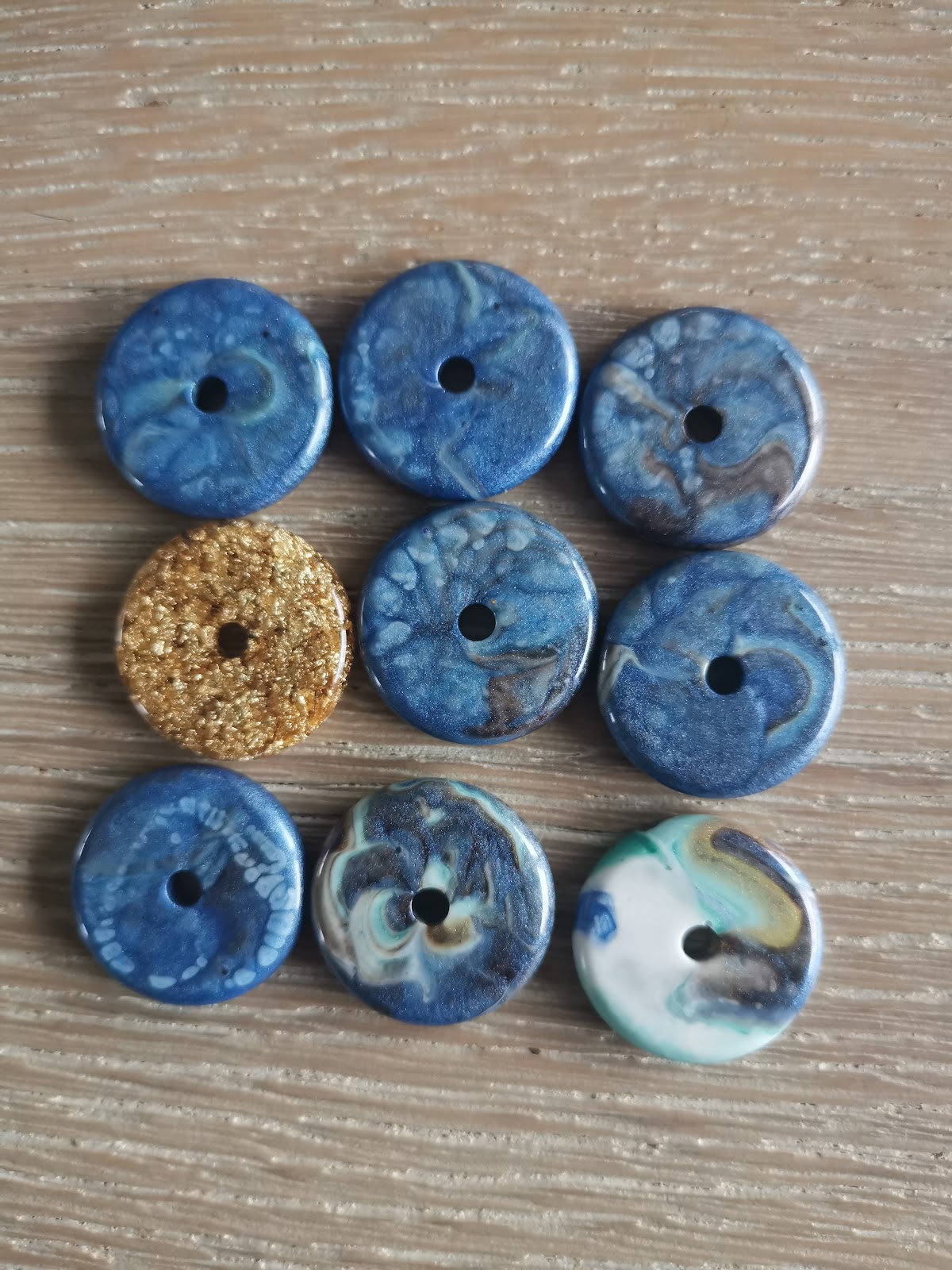 Nine finished donut-shaped resin beads on wood, mostly blue marble with one gold and one turquoise