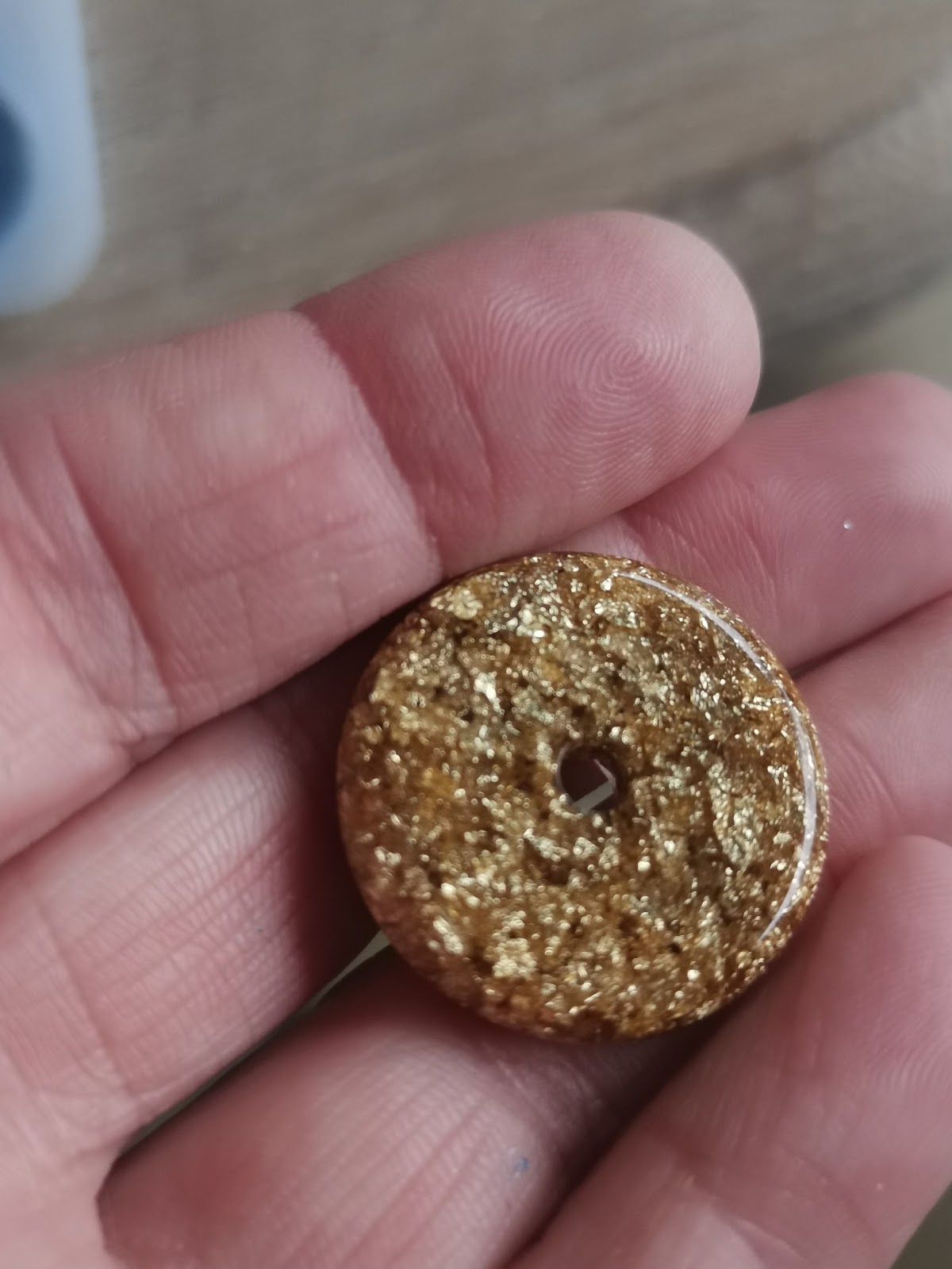 Close-up of a gold glitter resin bead with gold foil, held between fingers