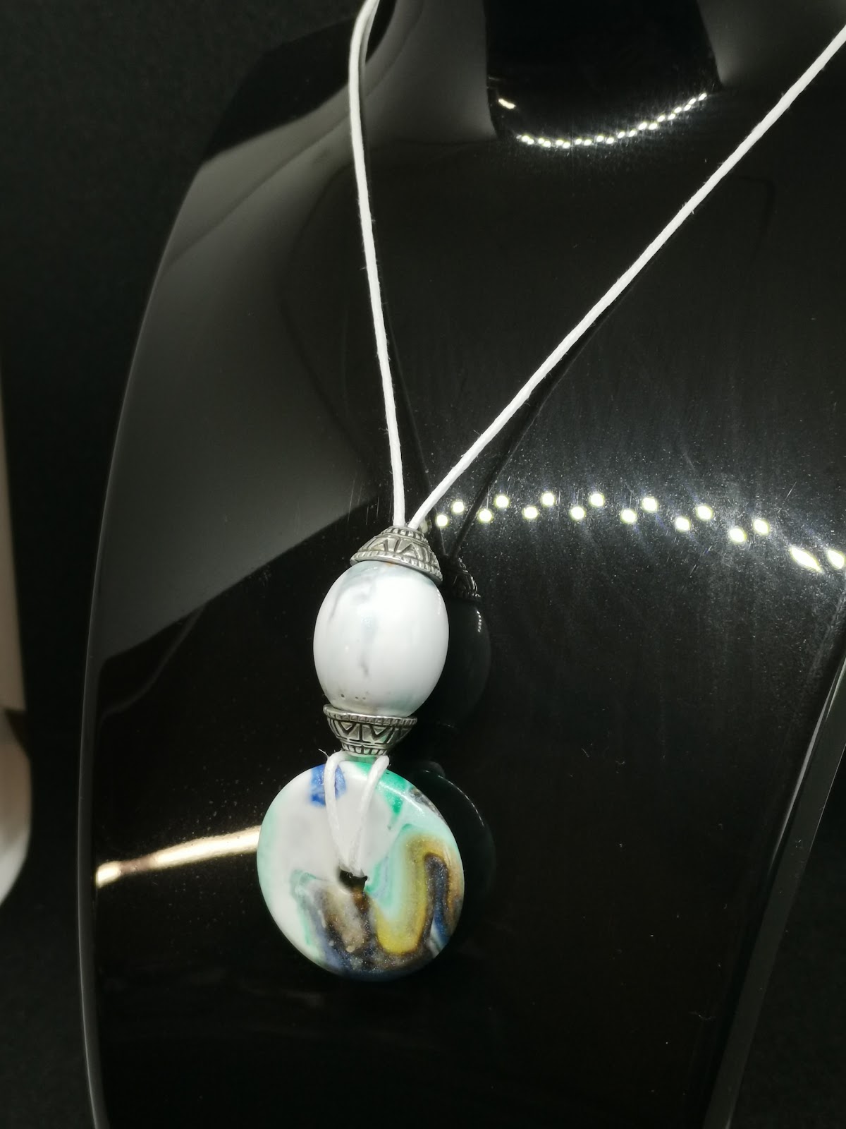 Necklace on bust: white cord with white oval resin bead and colorful blue-turquoise donut disc pendant