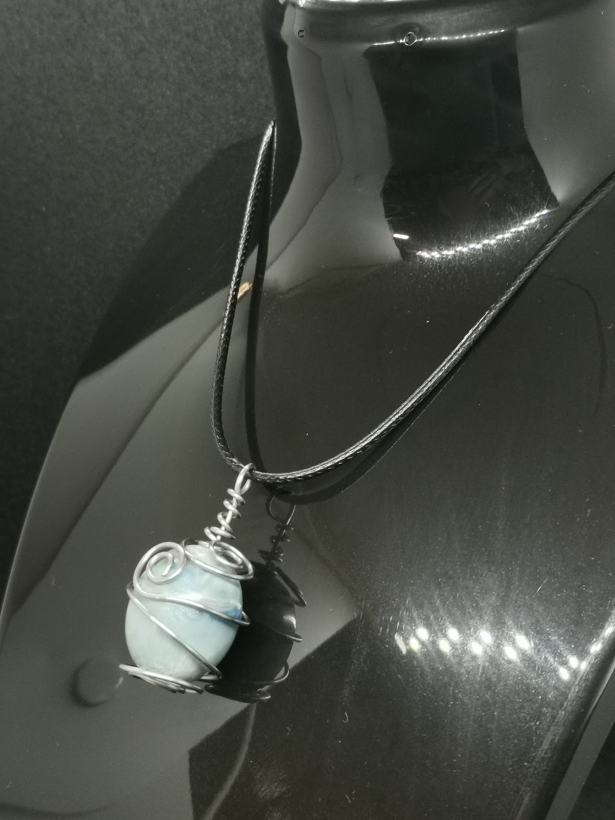 Necklace on bust: black leather cord with light blue round resin bead in silver wire cage wrap