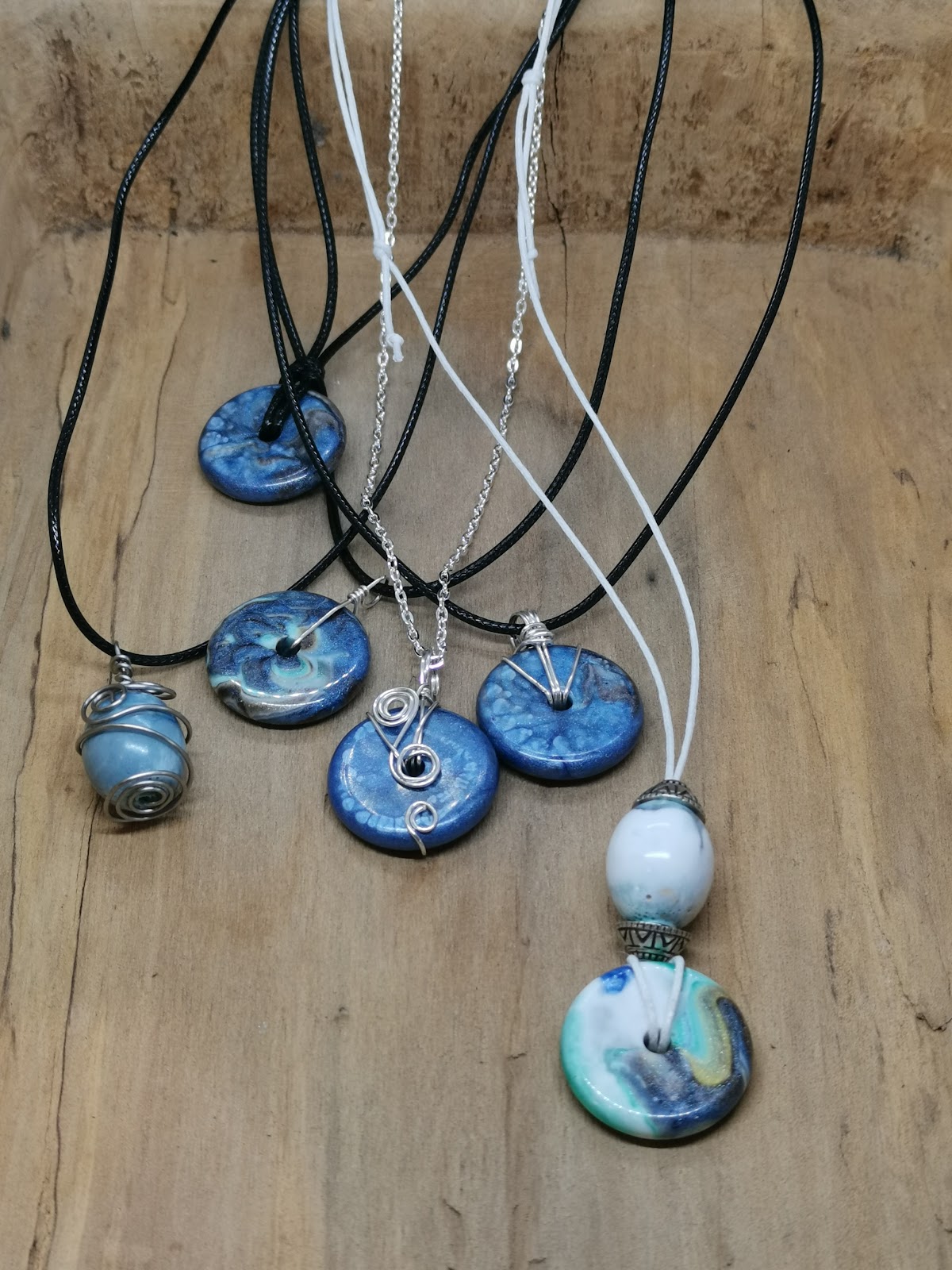 Groepsfoto van alle zes afgewerkte hars-juwelen kettingen op een houten ondergrond