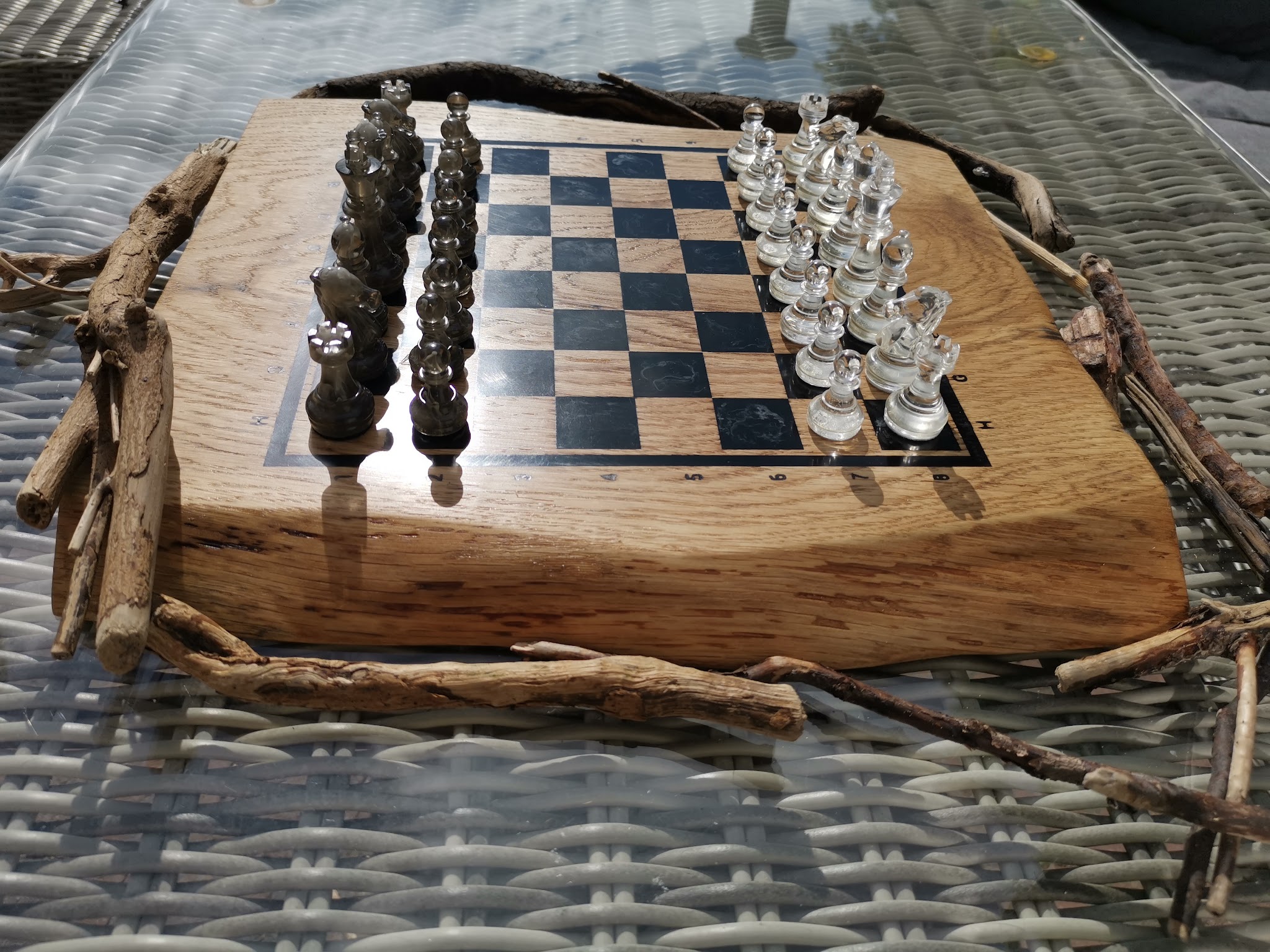 Afgewerkt schaakbord van eik en epoxy met twee sets gegoten resin schaakstukken gestyleerd op drijfhout buiten