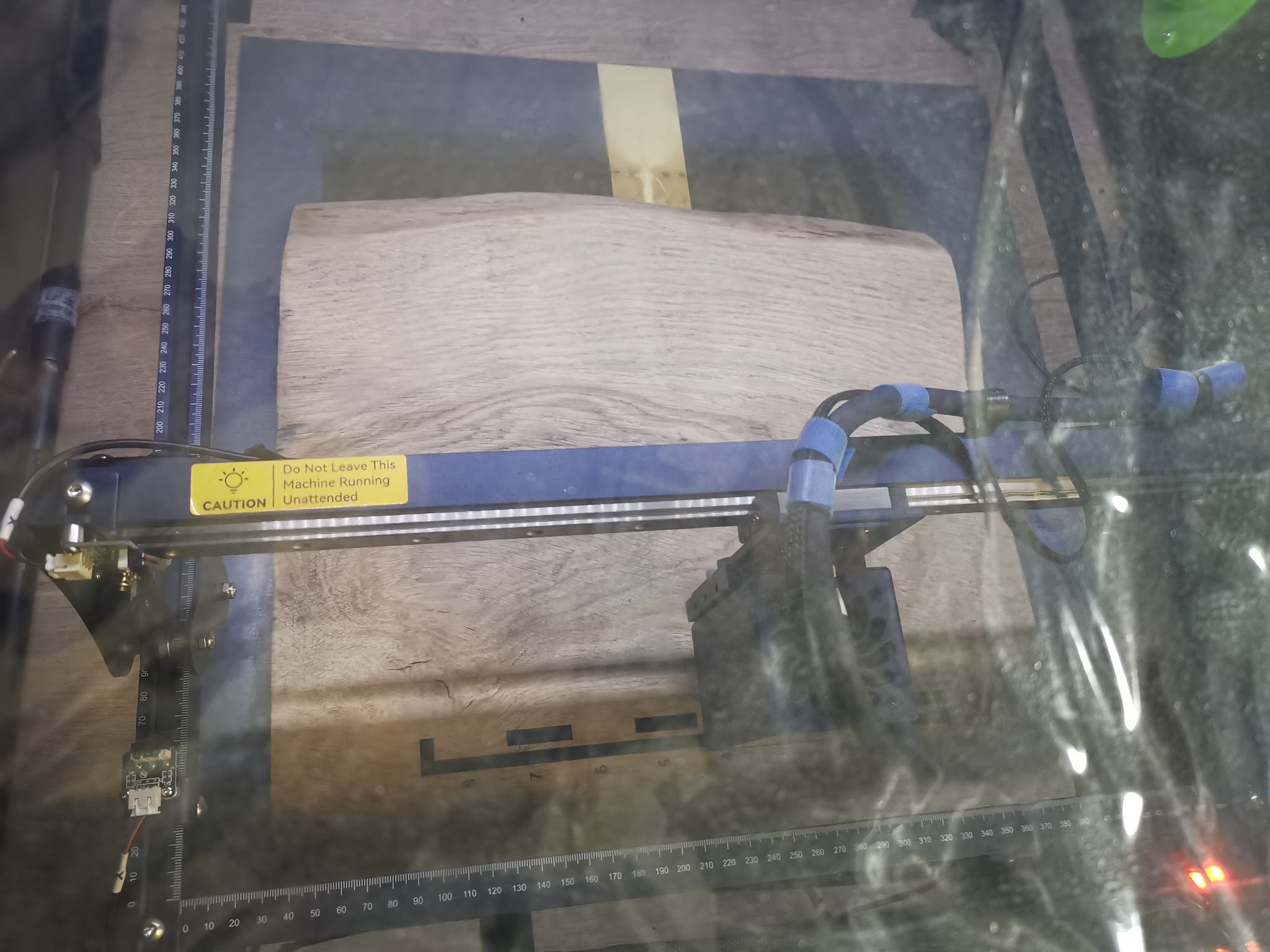 Eiken plank in lasergraveermachine met gele veiligheidslabels en blauw vacuümsysteem zichtbaar