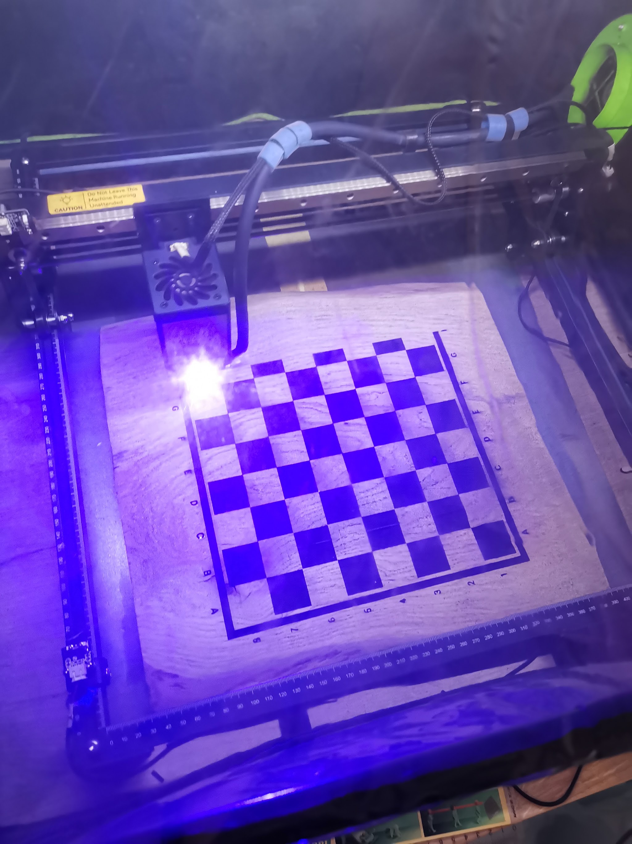 Blauwe laserstraal zichtbaar tijdens het inbranden van het schaakbordpatroon op de eiken plank