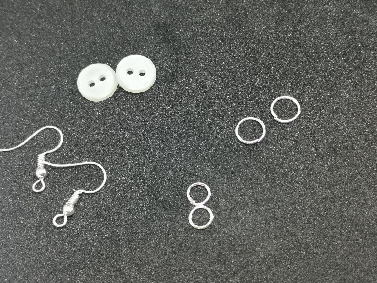 De onderdelen: 2 kleine witte 2-gaatsknopen, grote en kleine jumping rings en zilverkleurige oorhaakjes