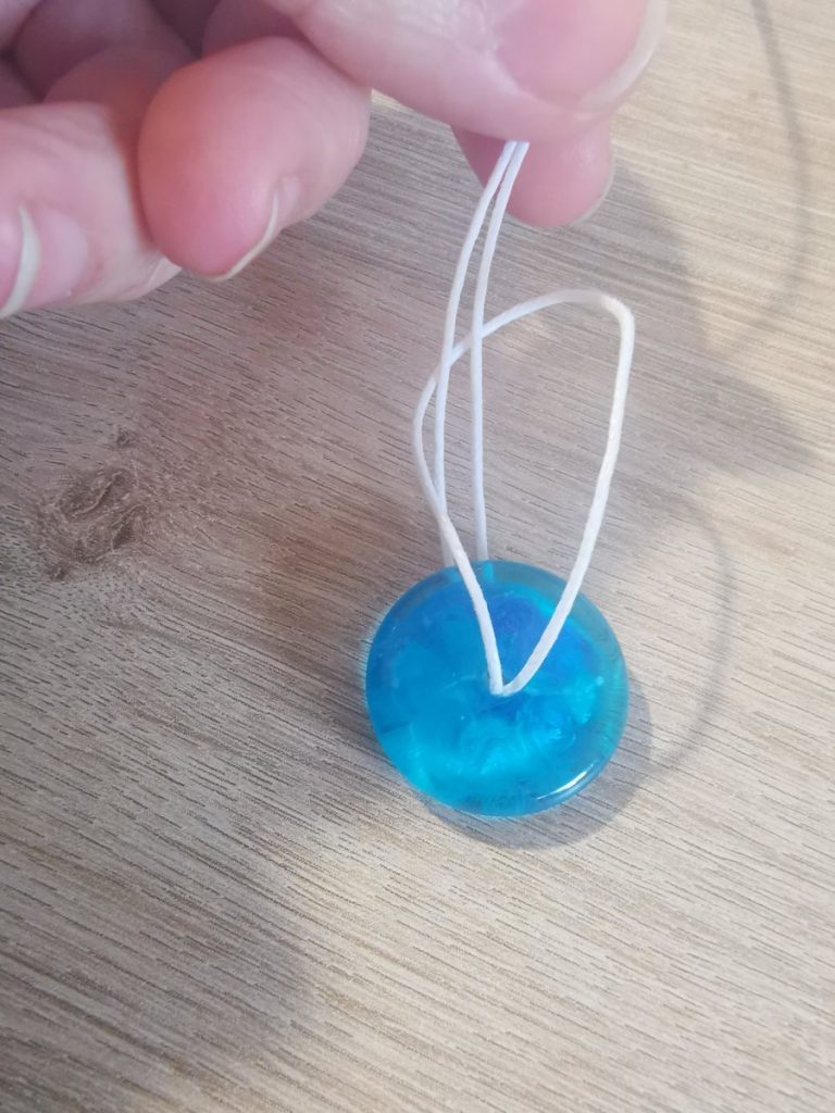 Het koord dubbel gelust door de harsdonut — twee draden lopen omhoog