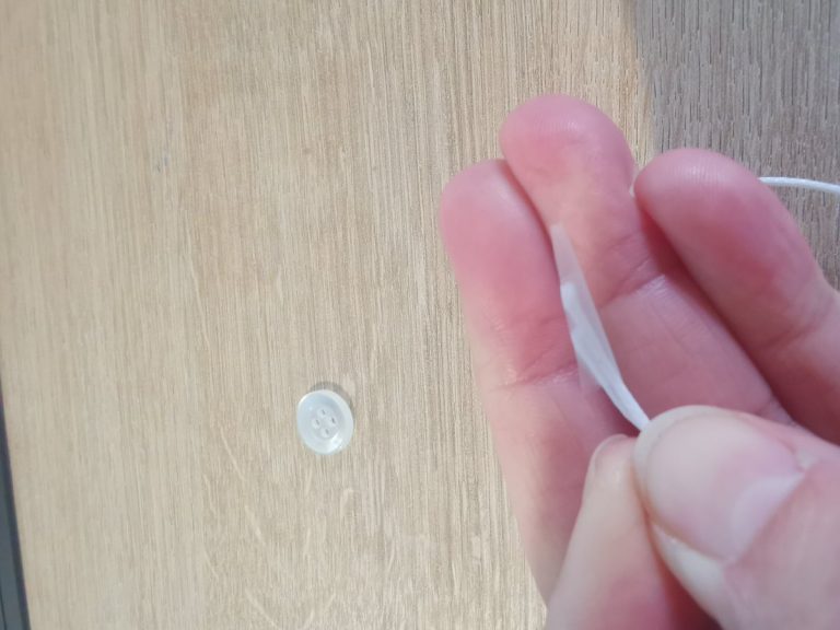 Techniek: het koord met behulp van plakband door één gaatje van een knoop rijgen